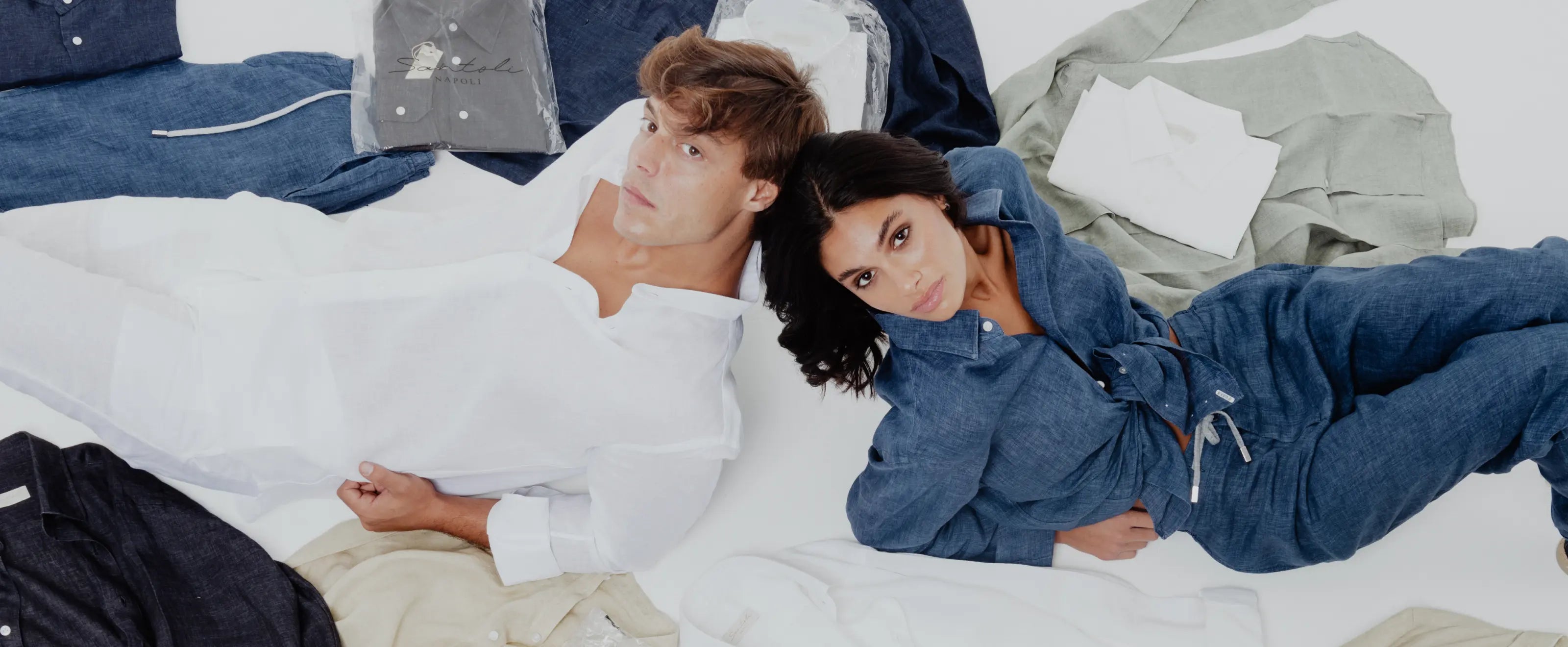 Two people lying on a bed surrounded by clothes